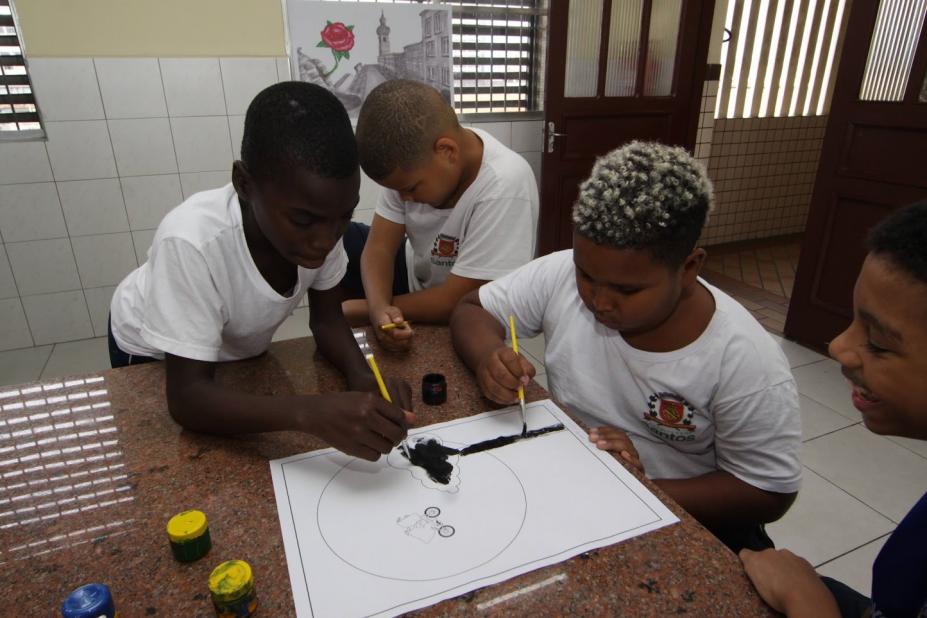 meninos estão pintando cartaz com pincel e tinta. #paratodosverem