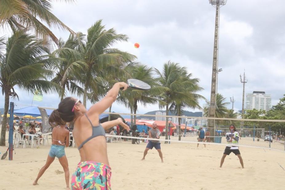 duas duplas jparticipam de um jogo na areia, com raquete e rede no meio. #paratodosverem