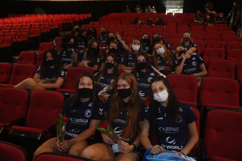 ATLETAS SEGURAM ROSAS. ELAS ESTÃO SENTADAS NA PLATEIA DE UM TEATRO. #PARATODOSVEREM