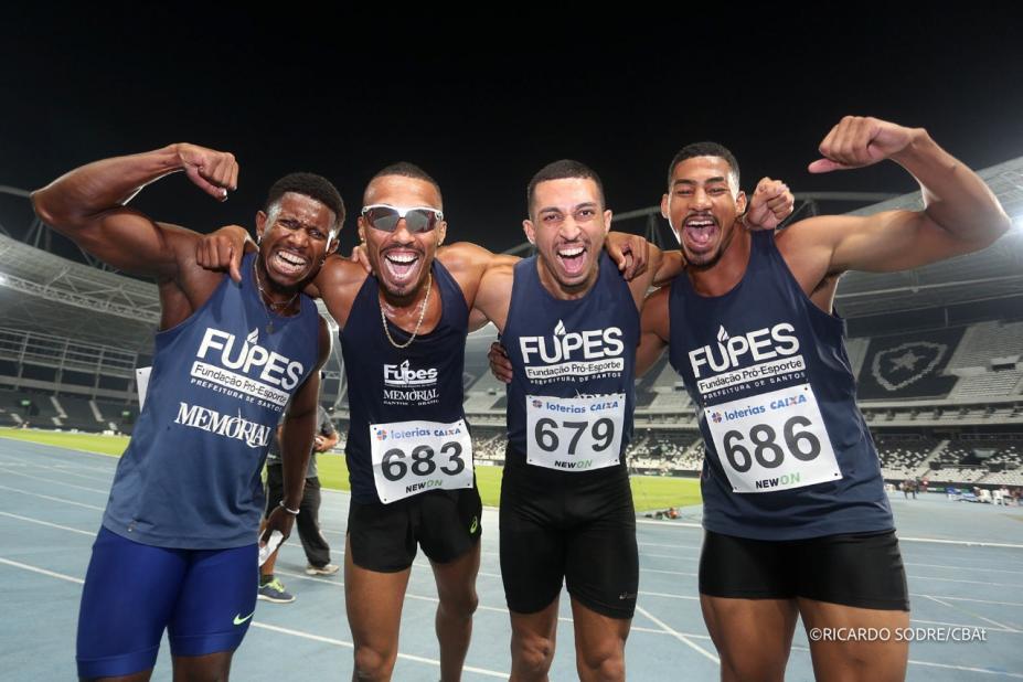 equipe de quatro atletas com uniforme da fupes. Eles estão abraçados posando para a foto. Os dois das pontas comemoram com os braços para o alto. #paratodosverem