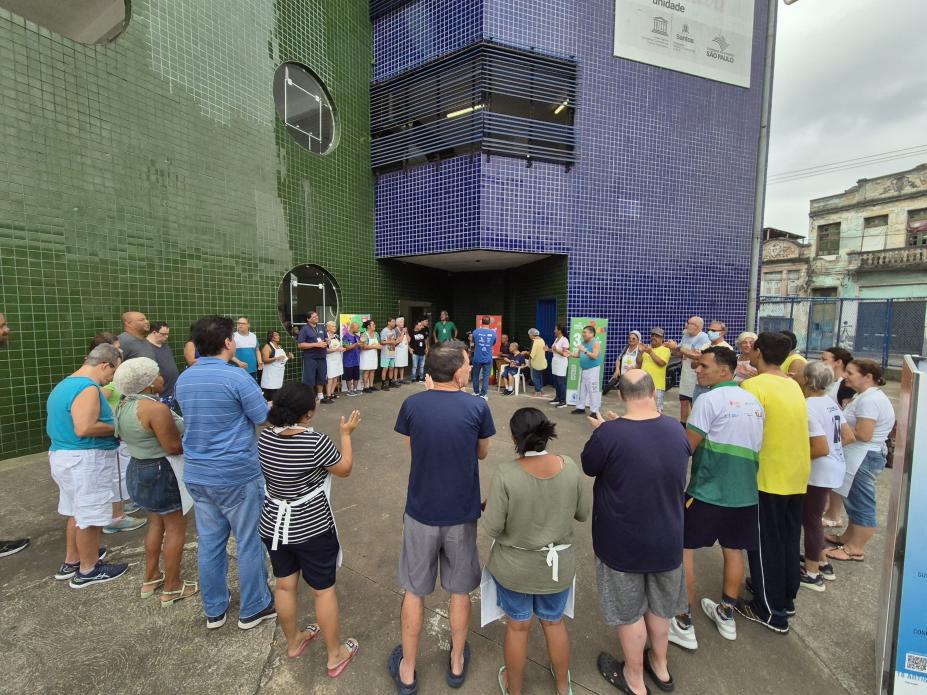 pessoas se reúnem em circulo diante de prédio. #paratodosverem 