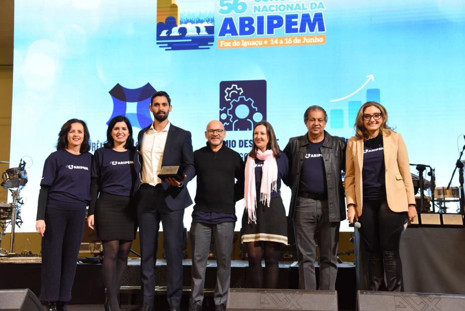 sete pessoas posam para foto em pé. O terceiro deles, da esq. p/dir. segura um troféu. #paratodosverem 