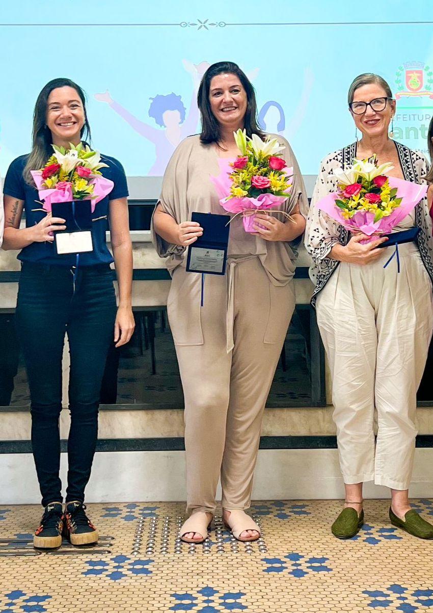 Rosane, Marilucy Fontes e Ingrid posam para foto segurando buquês de flores. #paratodosverem