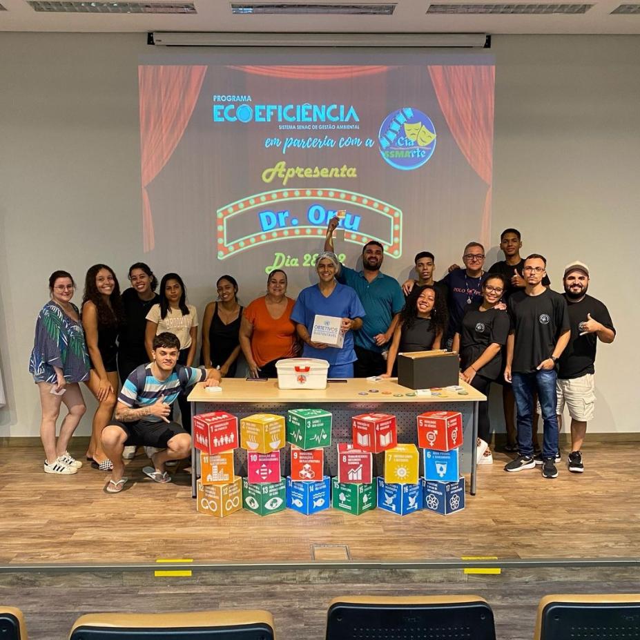 atores e alunos posam na frente de mesa com cubos indicando os objetivos do desenvolvimento sustentável #paratodosverem 