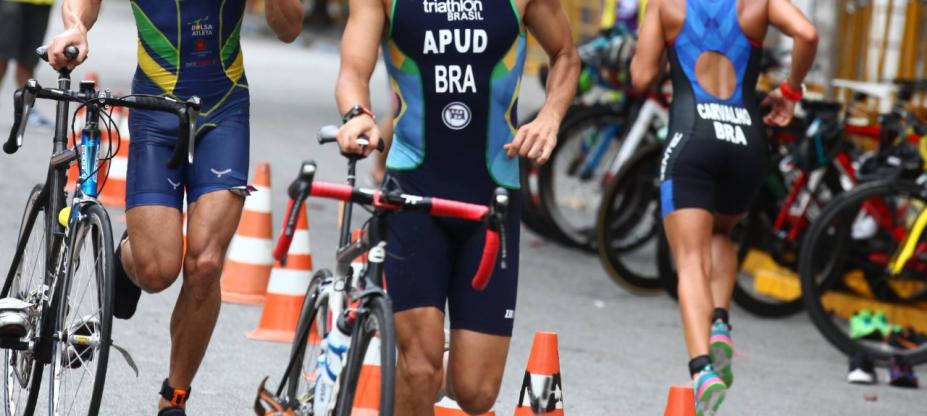 Imagem mostra parte do corpo de atletas correndo com a bicicleta do lado. #paratodosverem
