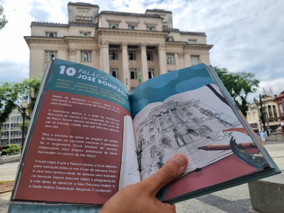 mão segura livro aberto em frente ao paço municipal. #paratodosverem