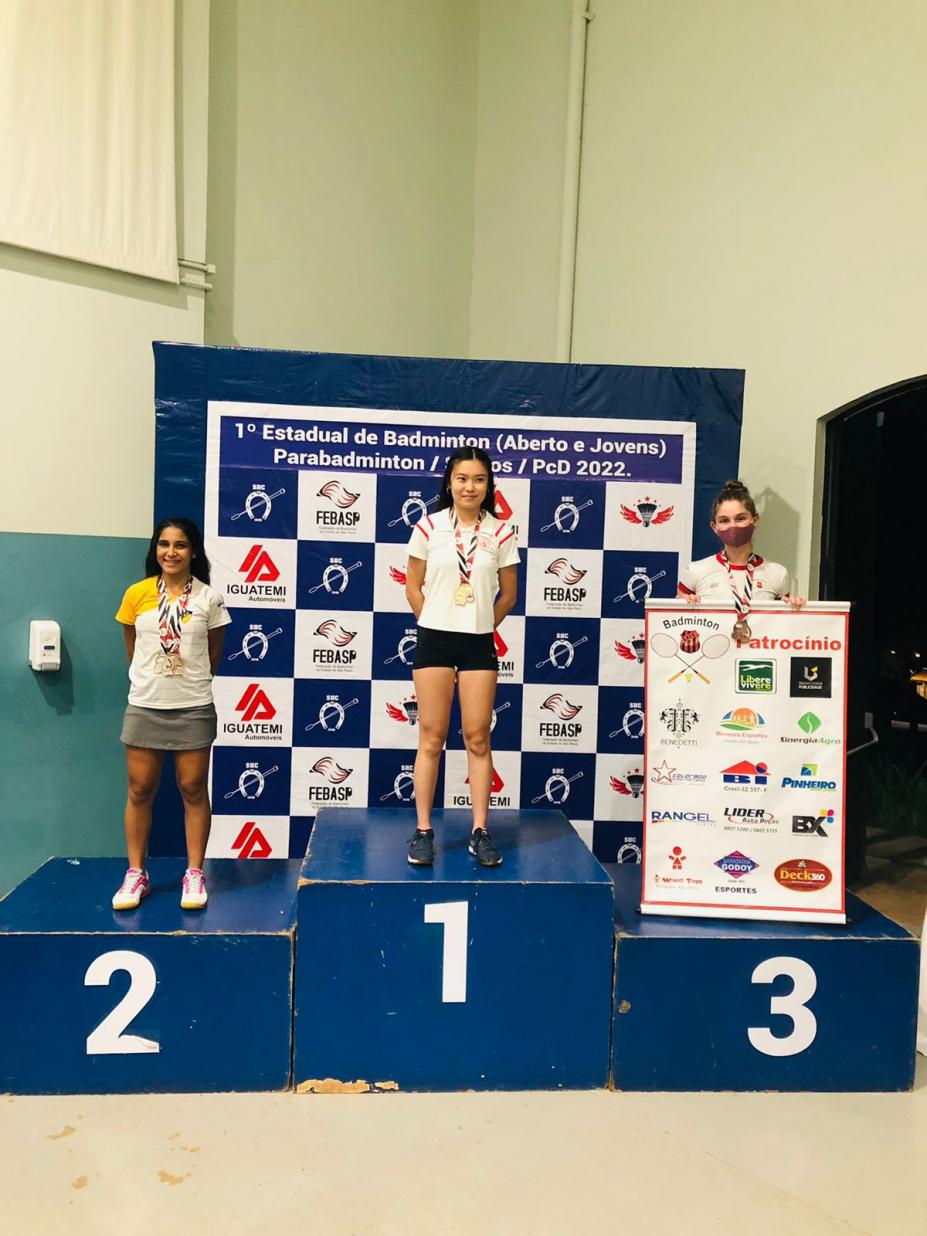 pódio com três mulheres. Thalia está no segundo lugar, ao lado esquerdo da foto. #paratodosverem