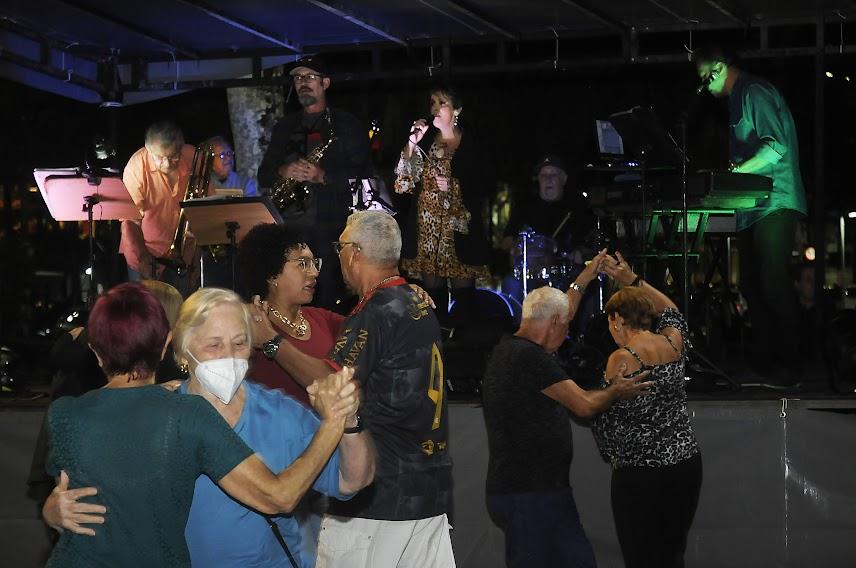 duplas danças no Baile na Praia ao som de banda que toda ao fundo num palco. #paratodosverem