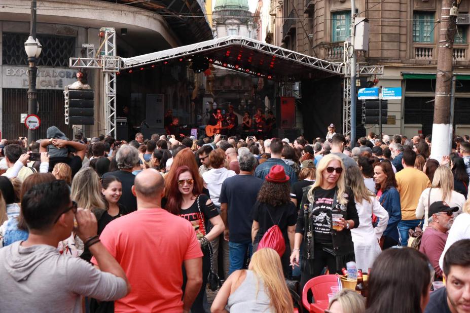 Público lota rua para assistir apresentação de banda em palco. #Pracegover