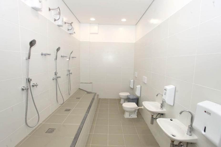 banheiro com itens acessíveis, como chuveiros, à esquerda, e pias e vasos à direita. #paratodosverem