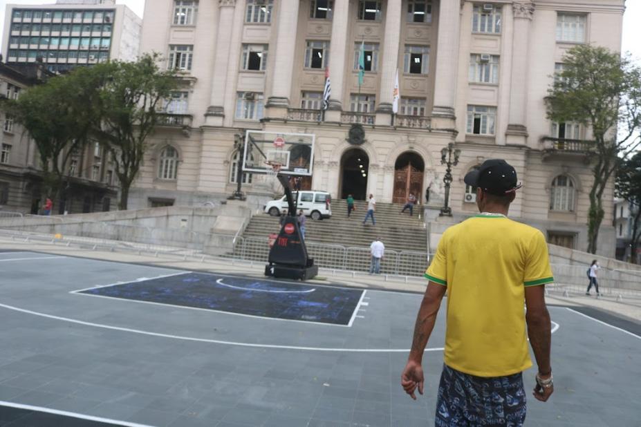 Jovem observa quadra de basquete 3x3 em frente a Prefeitura #paratodosverem