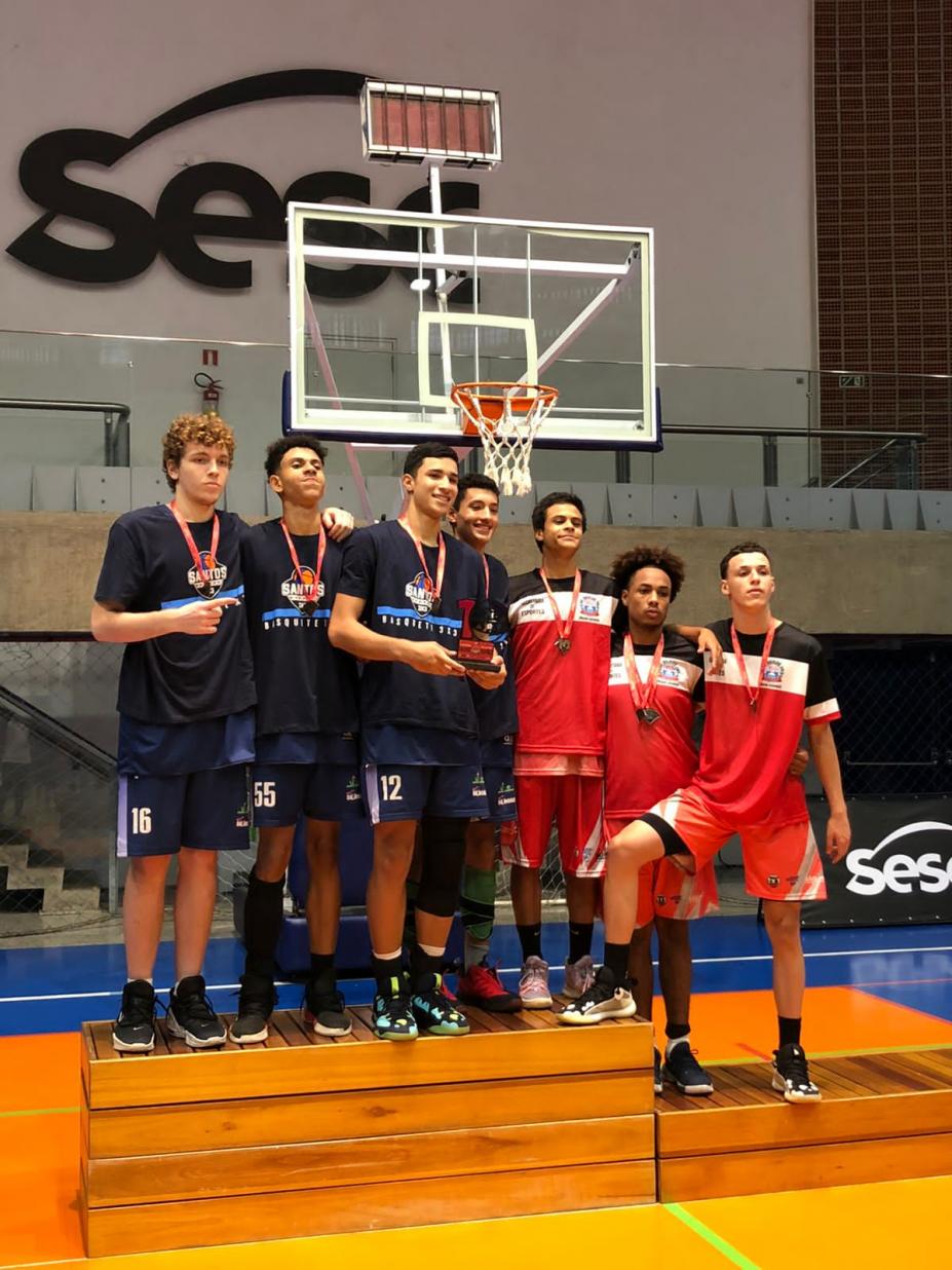 atletas estão no pódio diante de cesta de basquete. #paratodosverem