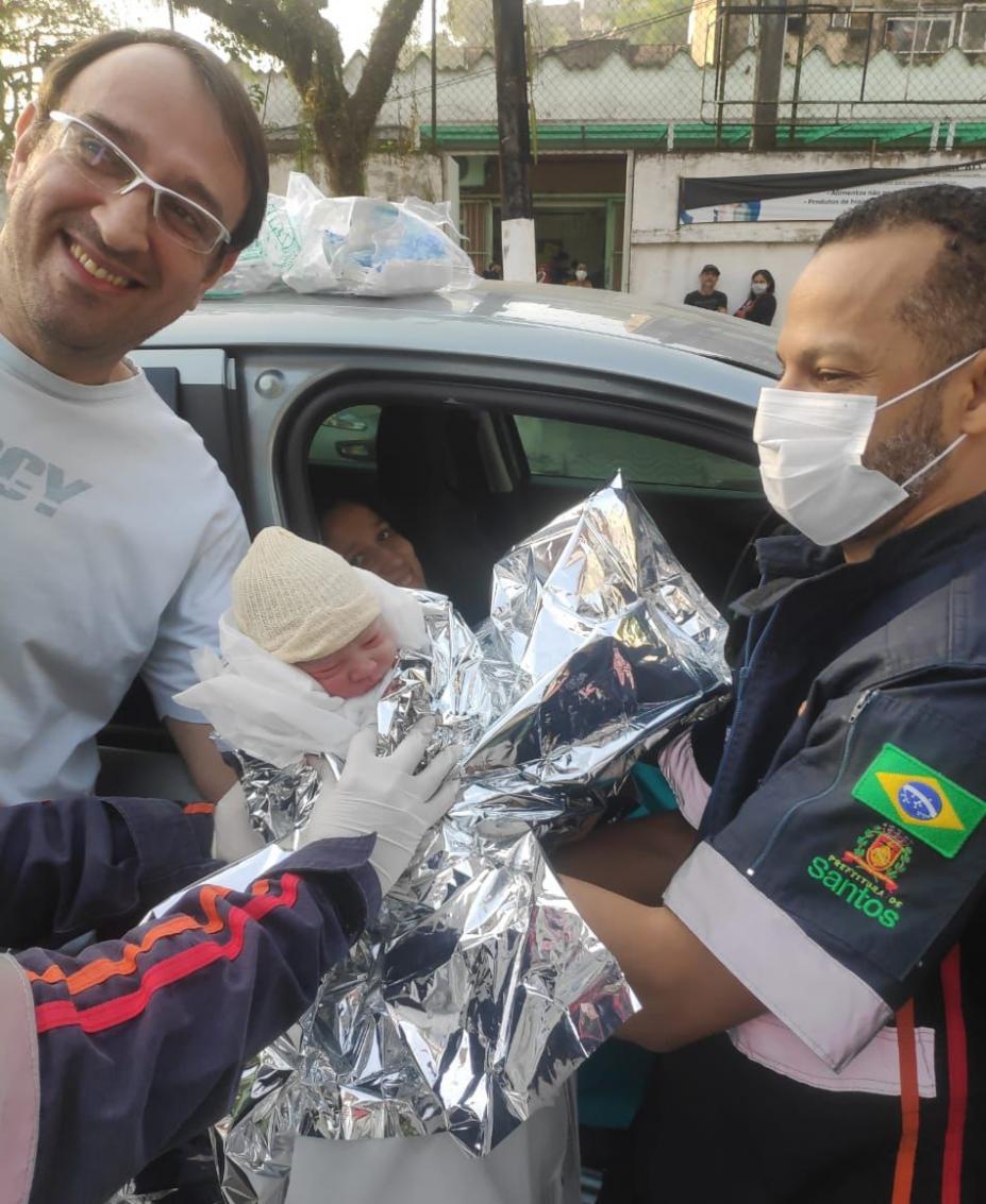 o pai e um atendente do samu seguram o bebê que está coberto por uma manta aquecedora. #paratodosverem