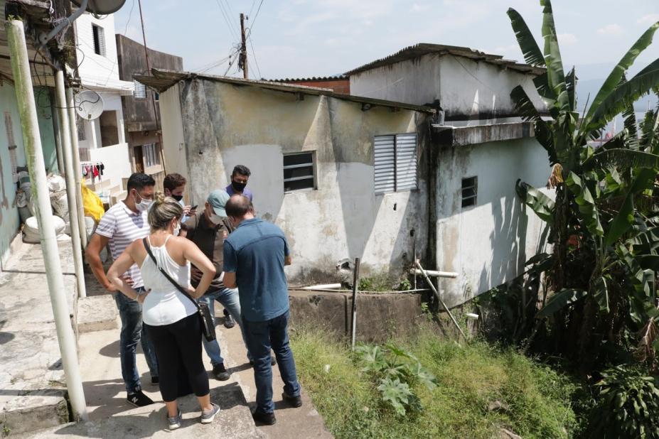 Grupo de pessoas está no alto de uma encosta ao lado de algumas casas. #Paratodosverem