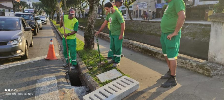 Operários preparam instalação de cobertura de boca de lobo em concreto. Eles estão em uma calçada ao lado de um canal. #paratodosverem