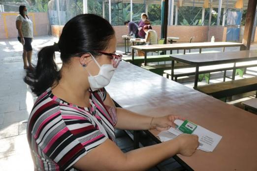 Mulher segura e olha para cartão bolsa-alimentação e papeis. #pracegover