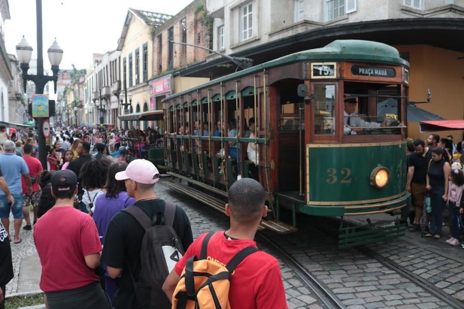 bonde circula em rua com grande público em torno. #paratodosverem 