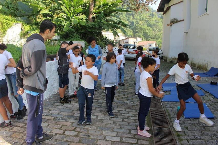 crianças uniformizadas estão se divertindo ao ar livre. Há colchonetes pelo chão. #paratodosverem