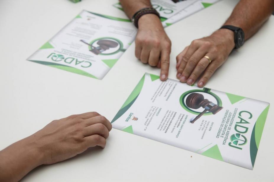 mãos estão apontando para folheto do cadoj que está sobre uma mesa. #paratodosverem