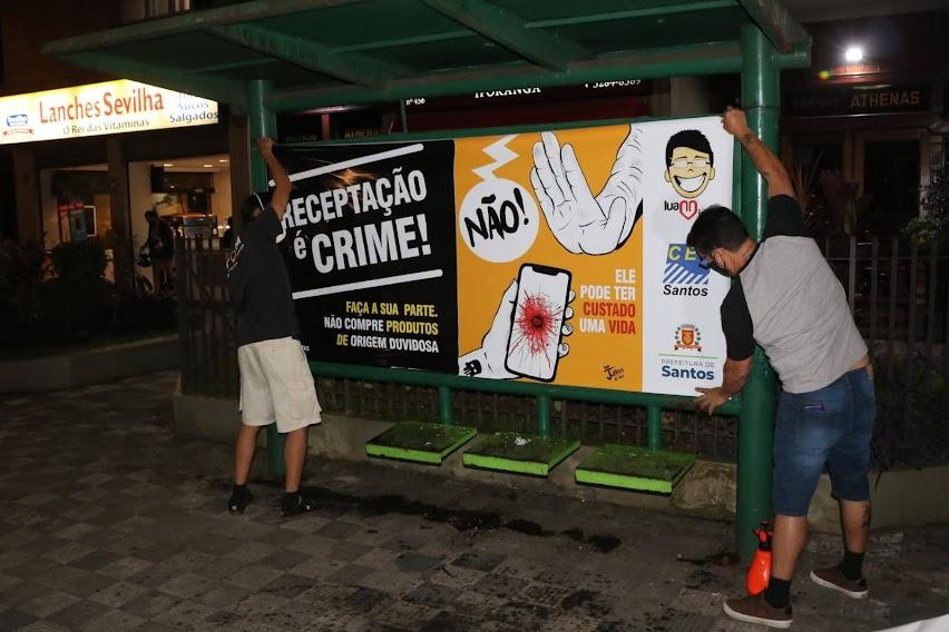 Dois jovens afixam cartaz em ponto de ônibus #paratodosverem