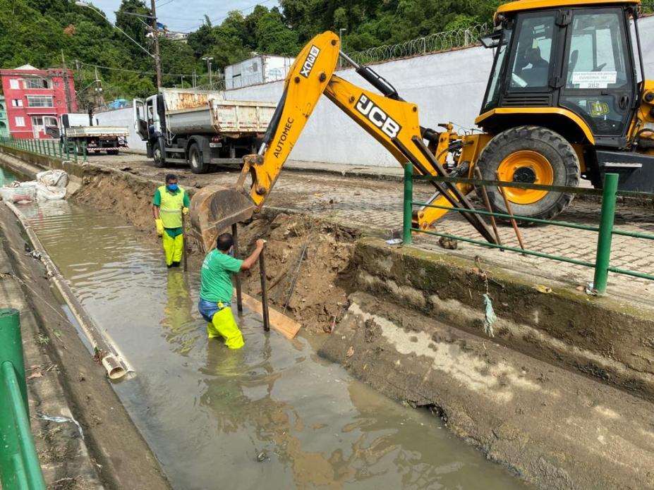 Retroescavadeira remove parte do talude. Há dois homens trabalhando dentro do canal. #Paratodosverem