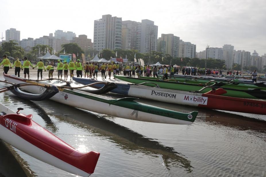 CANOAS HAVAIANAS VAZIAS ESTÃO PARADAS NA BEIRA DO MAR. aO FUNDO, EQUIPES UNIFORMIZADAS. #PARATODOSVEREM