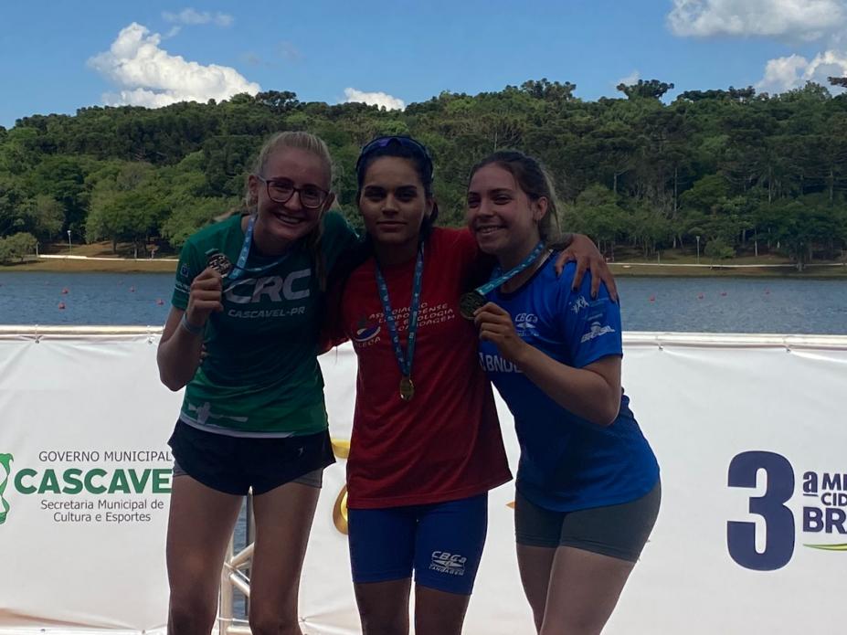 três atletas exibem medalhas com rio ao fundo #paratodosverem