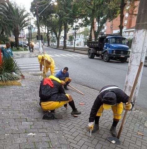 homens uniformizados raspam trecho de calçada. #paratodosverem