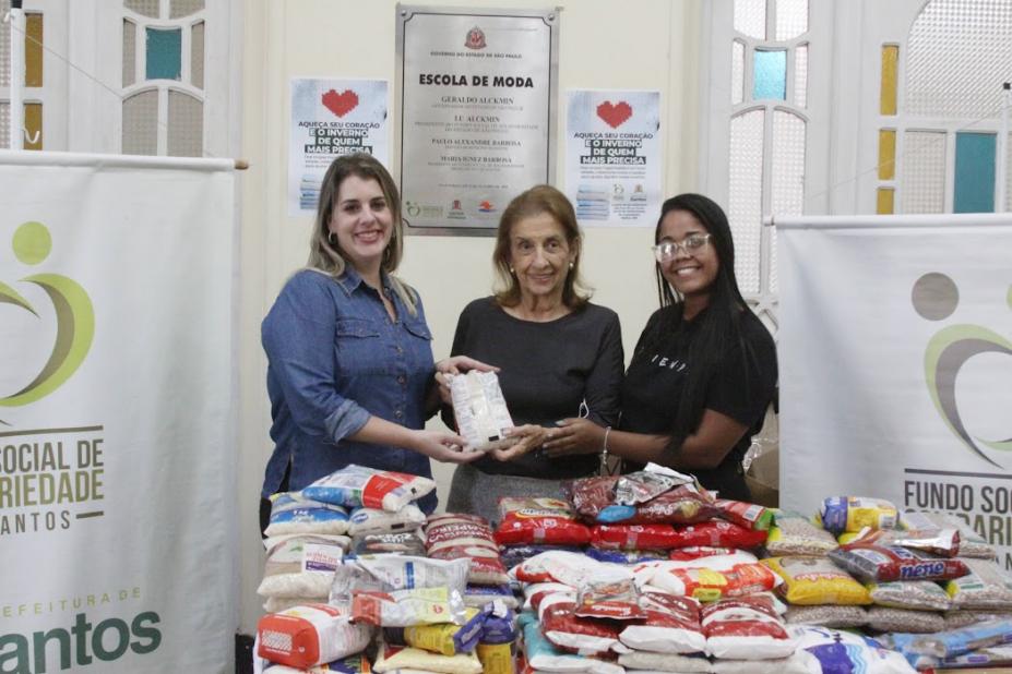 representantes do shopping e do fundo seguram alimento atrás de mesa cheia de alimentos #paratodosverem