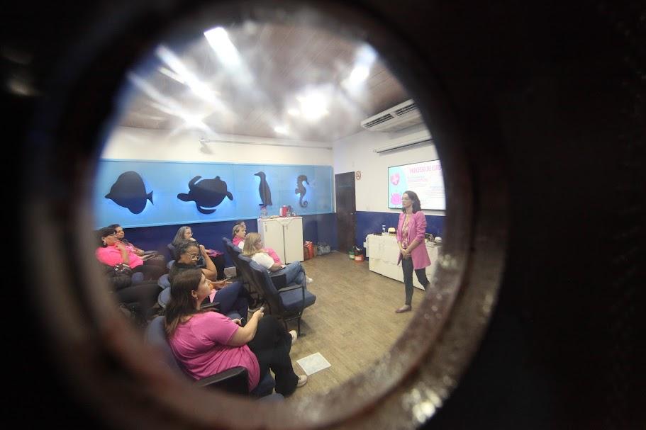 foto feita do lado de fora do auditório foca pequena abertura de vidro na porta por onde se vê a palestra ocorrendo no interior. #paratodosverem