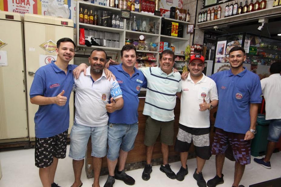 Homens abraçados em frente a balcão de restaurante. #paratodosverem