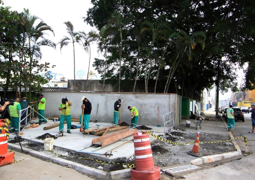 Várias pessoas trabalhando em uma praça localizada em uma esquina. #paratodosverem