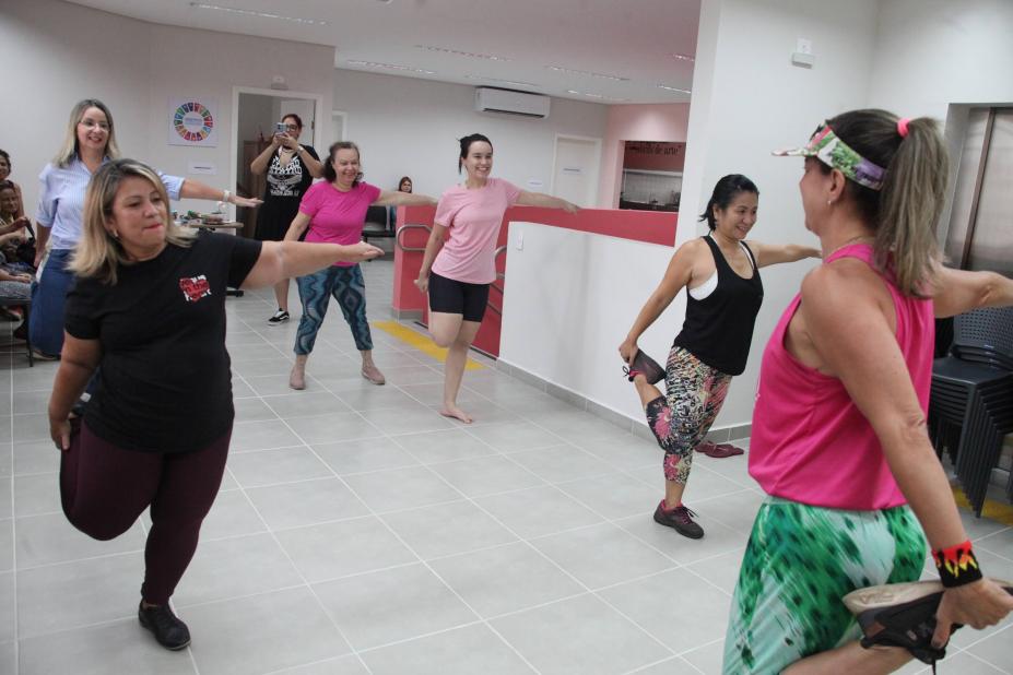 mulheres fazem alongamento com as pernas em salão. #paratodosverem 