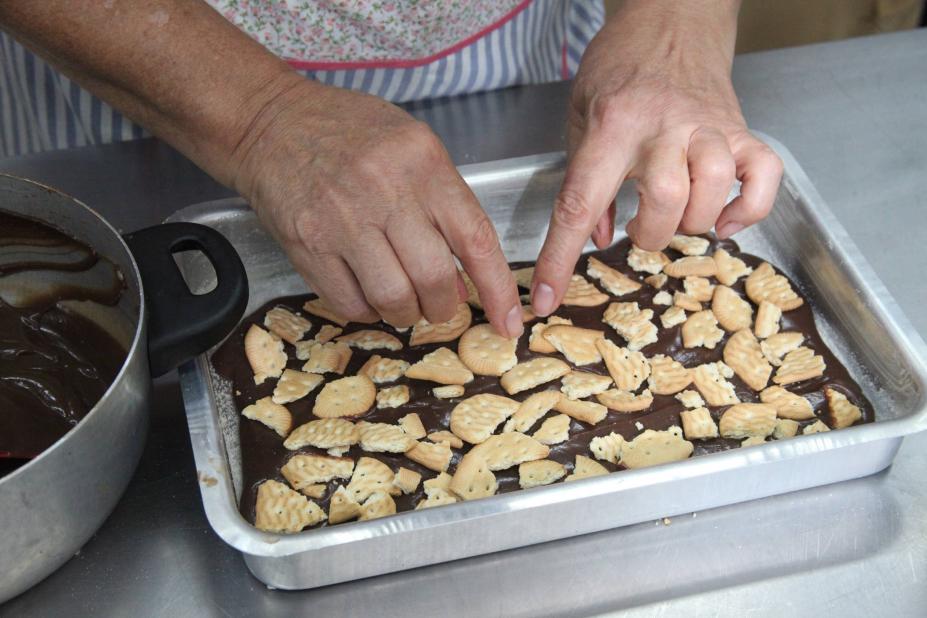 mulher colaca biscoitos sobre base de chocolate em forma. #paratodosverem