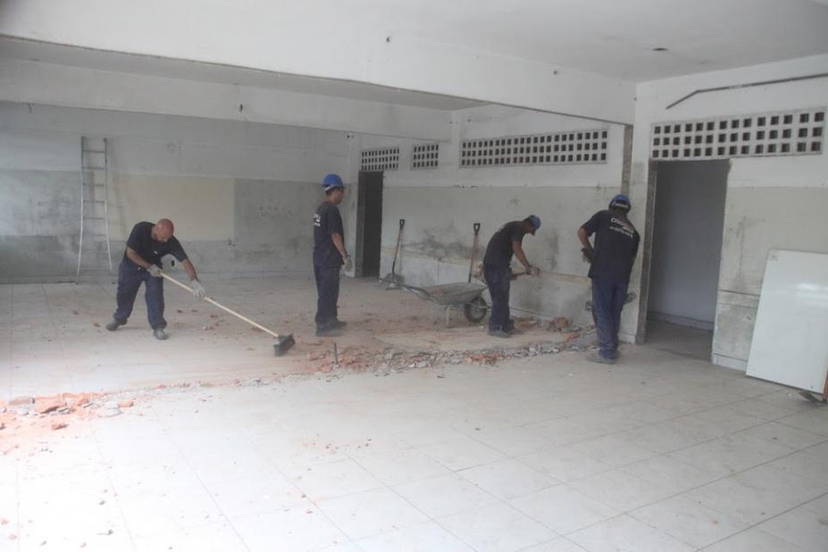 quatro homens uniformizados trabalham na parte de alvenaria de um salão. #paratodosverem 