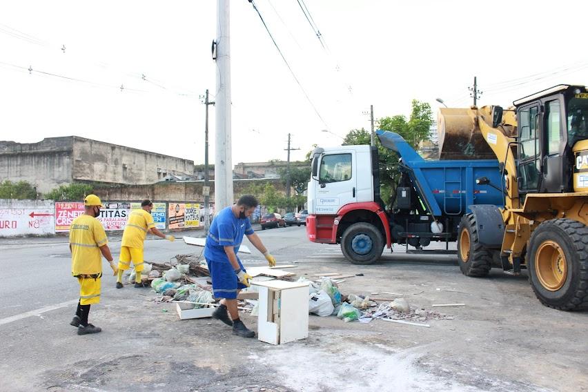 equipe de limpeza urbana está recolhendo entulho em calçada ao lado de trator e caminhão. #paratodosverem