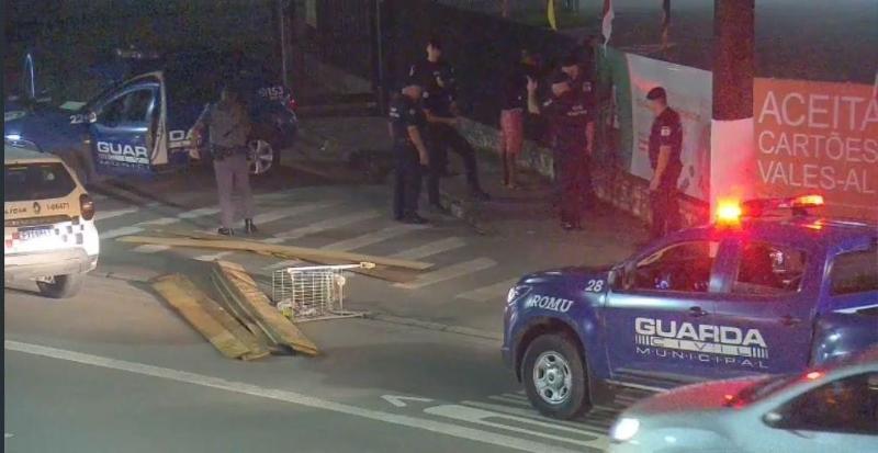 Madeiras e carrinho de supermercado jogados na avenida com viaturas da guarda no entorno. #paratodosverem