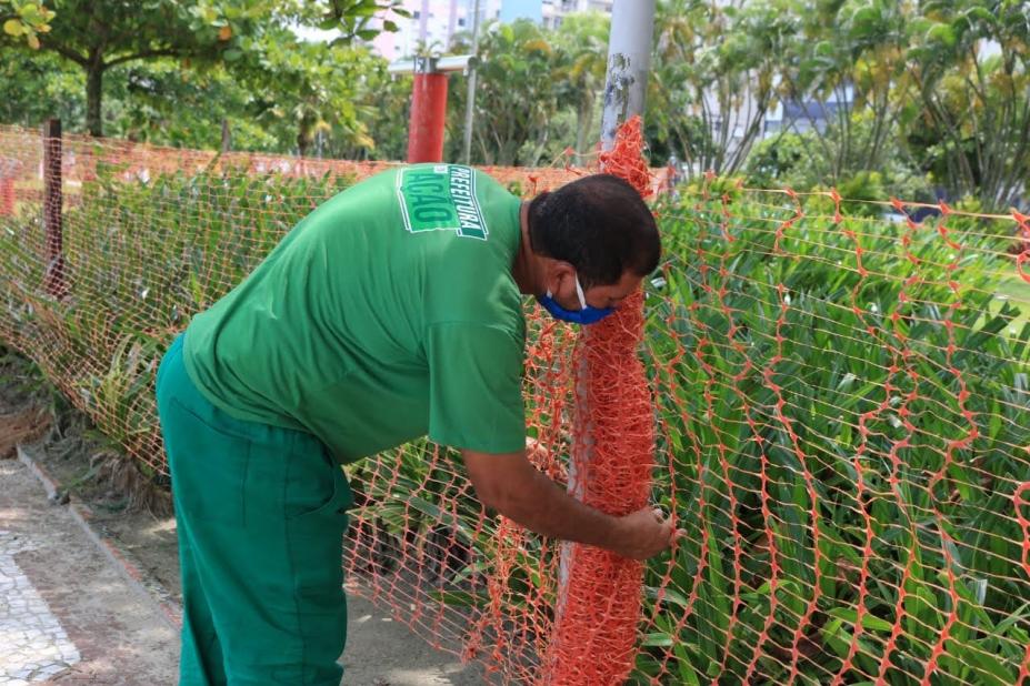 Funcionário instala cerca plástica diante do jardim da orla. #Paratodosverem