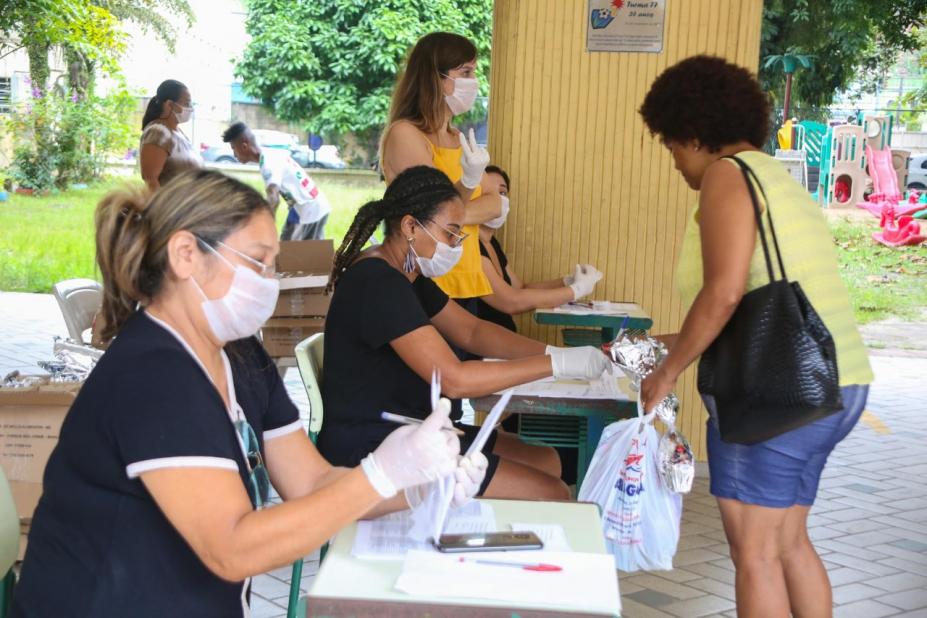 mulher se aproxima de mesas onde são feitos os cadastros para distribuição das cestas #paratodosverem 