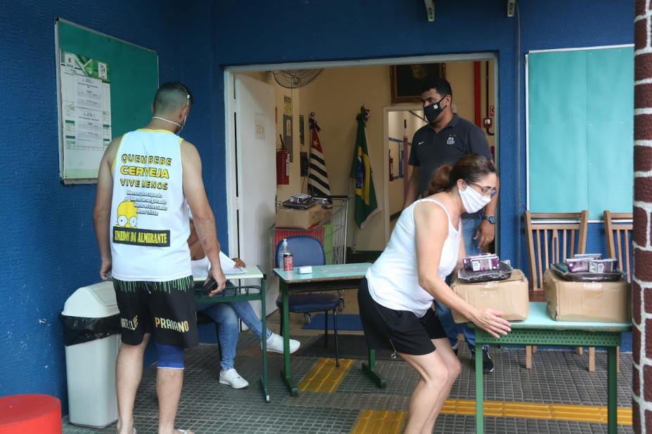 Mulher suspende cesta básica que está sobre uma mesa. Ao lado, um homem aguarda para ser atendido. #Paratodosverem