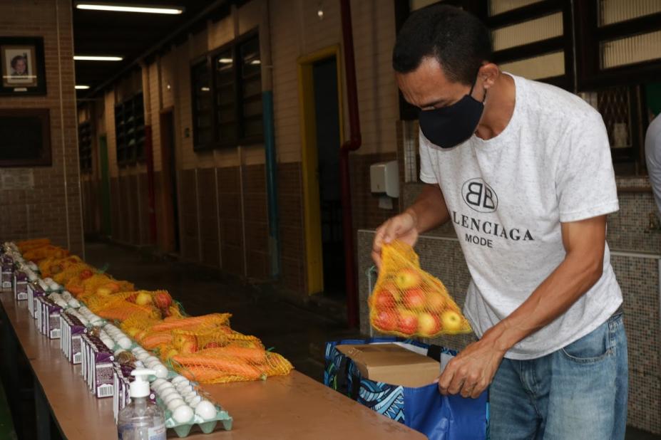 Homem está enchendo sacola com pacote de frutas frescas. #Paratodosverem