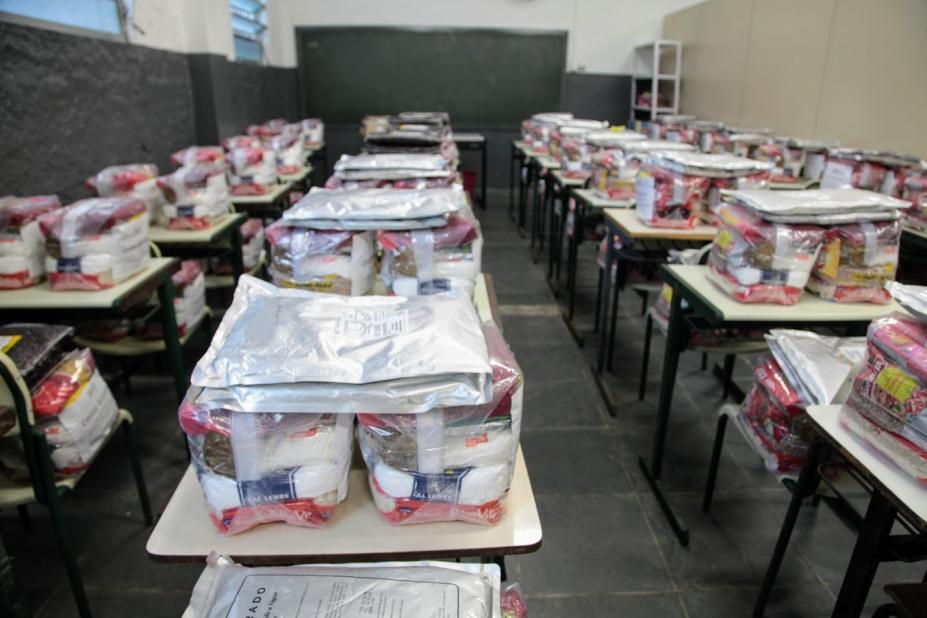 várias cestas básicas estão dispostas sobre carteiras escolares. #paratodosverem