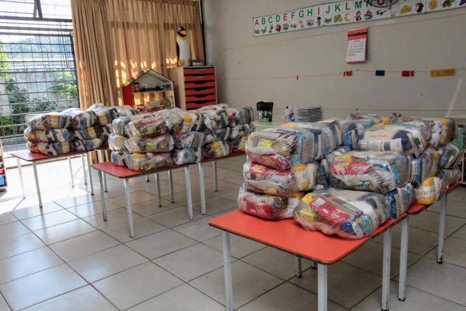 cestas básicas empacotadas estão dispostas sobre três longas mesas.#paratodosverem