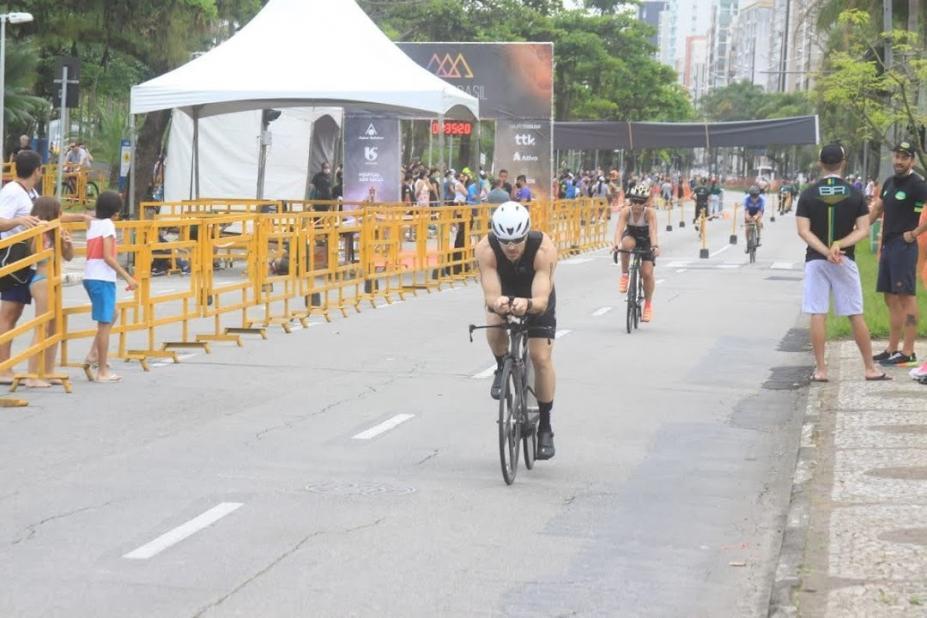 Ciclista pedala pela avenida da orla durante competição com outros atletas ao fundo. #pratodosverem