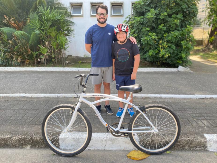 Pai e filho posam na frente da bicicleta. #Paratodosverem