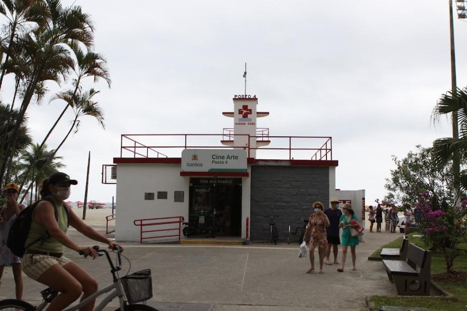Fachada do Cine Arte Posto 4 na orla com pessoas passando em volta e ciclista em primeiro plano. #pratodosverem
