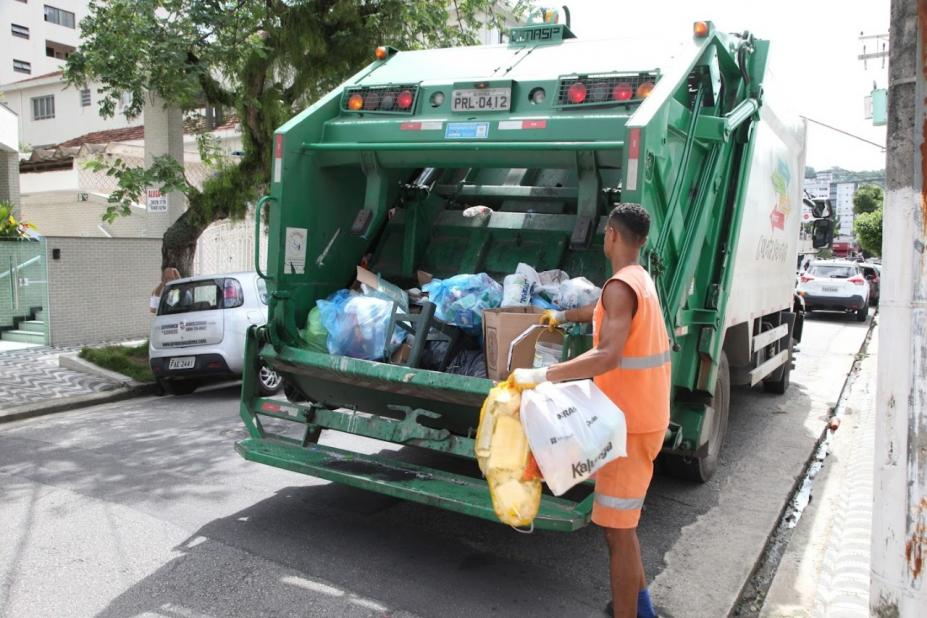homem está colocando sacos de lixo dentro de caminhão compactador que está na rua. #paratodosverem