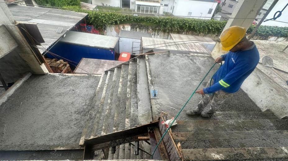 homem segura mangueira para molhar concretagem feita em escada entre pavimentos de uma obra. #paratodosverem 