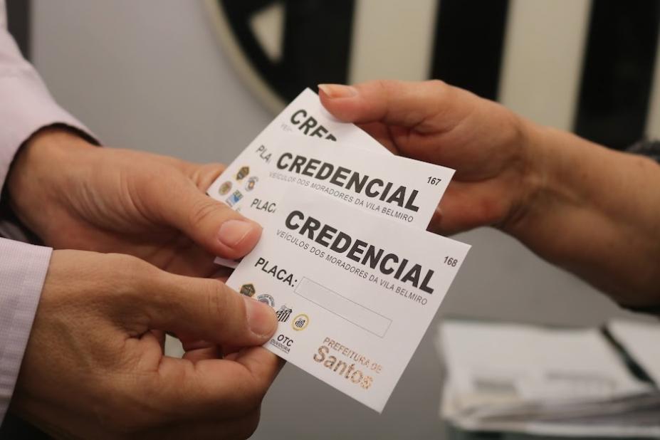 duas mãos de homem e uma de mulher seguram papeis onde se lê credencial ao mesmo tempo. #paratodosverem