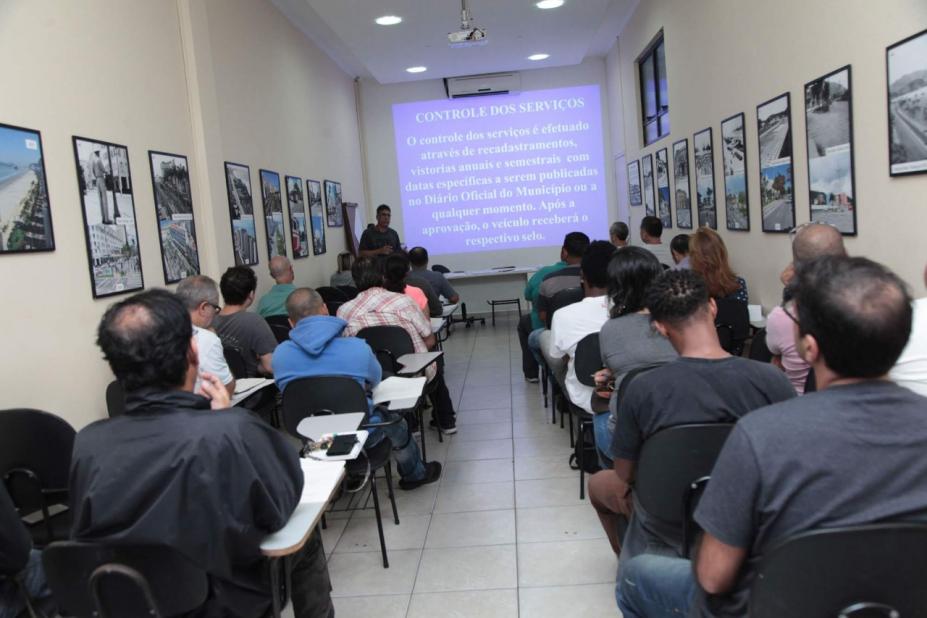 Homens estão sentados em sala de aula. #Paratodosverem